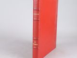 an old red book sitting on top of a table next to a white wall