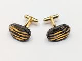 two pairs of gold and black striped cufflinks on a white surface