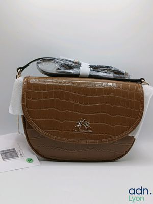 un sac à main marron et blanc, sur lequel sont posées des lunettes de soleil, posé sur une surface blanche