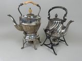 two silver teapots and a kettle on stands on a white surface