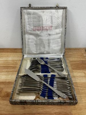des couverts dans un coffret en argent posé sur une table en bois ornée d'un ruban bleu