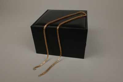 une boîte noire surmontée d'une chaîne dorée, posée sur une surface blanche