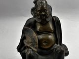 une statue représentant un homme assis sur une chaise, tenant un éventail