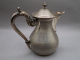 an antique silver coffee pot with a handle on a grey background