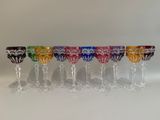 six verres à vin colorés alignés en rang sur une surface blanche