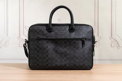 a black coach laptop bag sitting on top of a wooden table