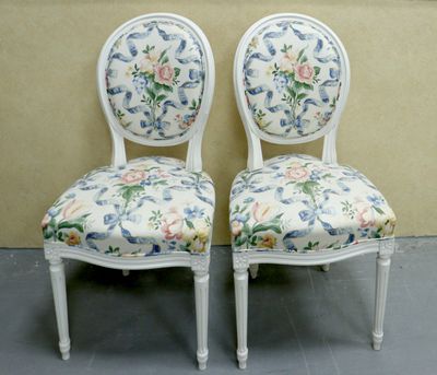 two white chairs with floral upholstered seats against a beige wall