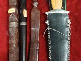 trois types de couteaux différents et un étui à couteau posés sur un tissu rouge