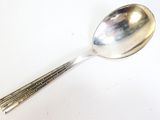une cuillère en argent à long manche posée sur une surface blanche