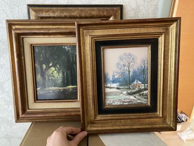 a person holding two framed pictures on a table