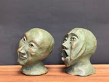pair of green ceramic sculptures of faces on a wooden table