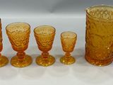 five glasses and a pitcher sitting on a table