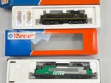 trois trains miniatures dans leurs boîtes, posés sur une table blanche
