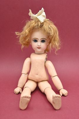 une petite poupée assise par terre, avec un nœud sur la tête