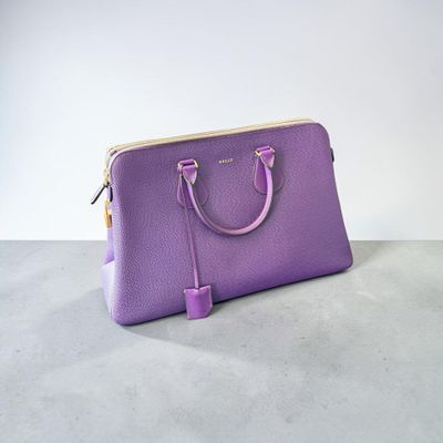sac à main en cuir violet posé sur une surface en béton, avec un mur blanc en arrière-plan
