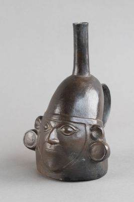 un vase noir orné d'un visage, posé sur une table