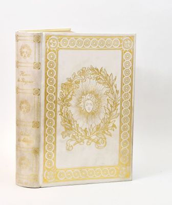 an old book with a gold and white cover on a white surface