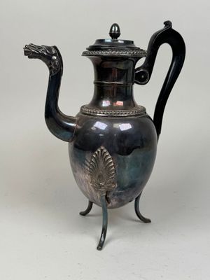 a silver tea pot with a peacock handle on a stand