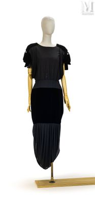 mannequin vêtu d'une robe noire, posé sur un socle en bois, devant un fond blanc