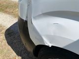 a small white car with a broken front bumper on the side of the road
