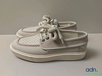 des chaussures bateau blanches avec des lacets blancs, posées sur une surface blanche