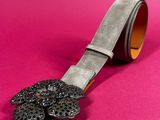 black leather belt with a flower buckle on a pink background
