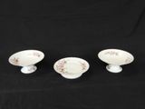three small white dishes with floral designs on them on a black background