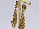 pair of gold and emerald earrings on a wooden stand