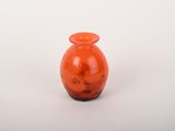 un petit vase en verre orange posé sur une surface blanche