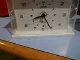 une horloge blanche posée sur une table, à côté d'une tasse rouge