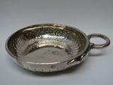 une assiette en argent antique avec une poignée sur une surface blanche