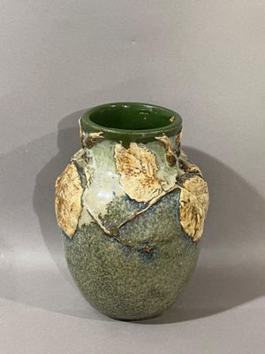 un vase vert orné de feuilles, posé sur une table