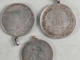 three silver coin pendants on a white surface
