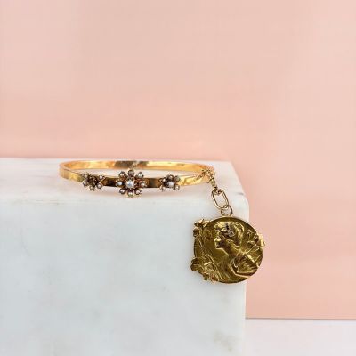 a gold bracelet with a coin charm on top of a marble block