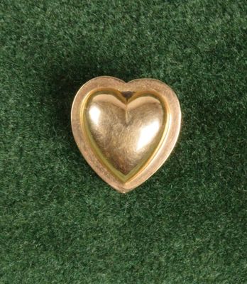 broche dorée en forme de cœur posée sur un tapis vert, sur fond vert