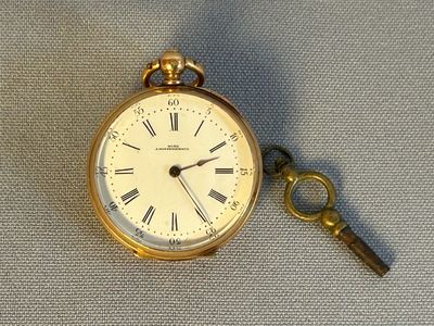 une montre de poche en or et une clé posées sur un tissu bleu