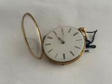 une montre de poche en or avec un cadran blanc sur une surface blanche