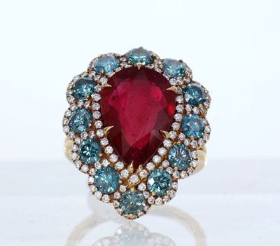 a close up of a ring with a red stone surrounded by blue and white diamonds