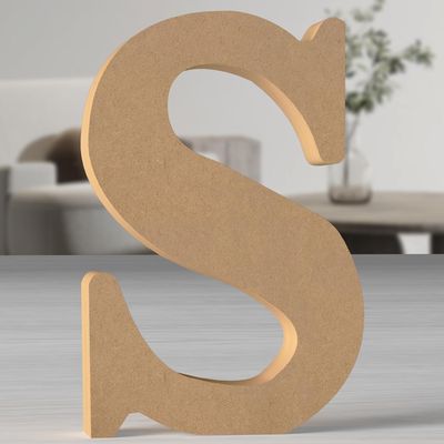 a wooden letter s on a table with a vase in the background