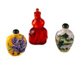 trois bouteilles en verre de couleurs différentes, ornées de motifs, posées sur une surface blanche