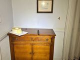 a wooden dresser in the corner of a room with a picture on the wall