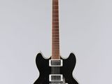 une guitare électrique noire posée sur une surface blanche