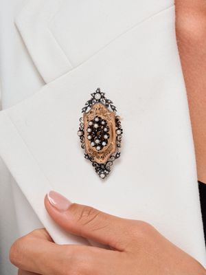 une femme vêtue d'un blazer blanc, avec une broche noire et dorée à la revers