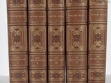 six old books are lined up in a row on a table