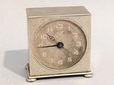 une petite horloge argentée posée sur une surface blanche