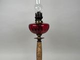 une lampe à huile à l'ancienne, dotée d'un abat-jour en verre rouge et posée sur un socle en bois