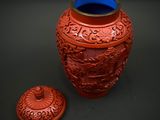 a red vase with a blue lid sitting next to it