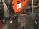 une soudeuse orange et noire dans un garage, à côté d'autres équipements