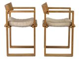 pair of wooden chairs with beige cushions on them against a white background