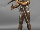 statue en bronze représentant un homme muni d'une pioche, posée sur un socle en bois